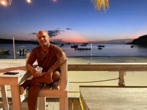 A man sitting at a table on the beach at sunset.