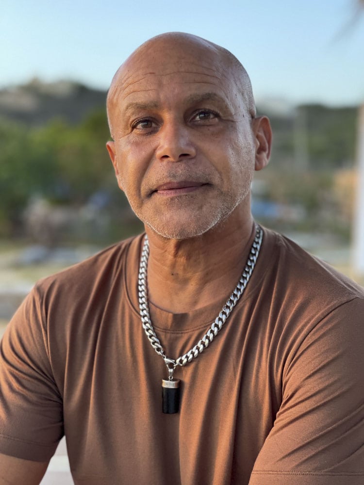 A bald man wearing a brown shirt and a chain necklace.